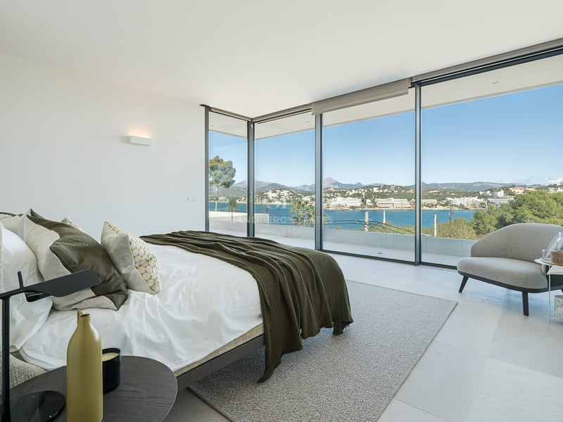 Chambre moderne avec baies vitrées du sol au plafond donnant sur une baie bleue et des montagnes.