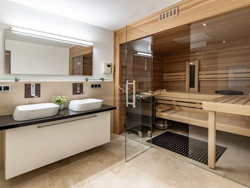 Salle de bain luxueuse avec sauna en bois intégré, porte vitrée et double vasque sur plan de travail noir.