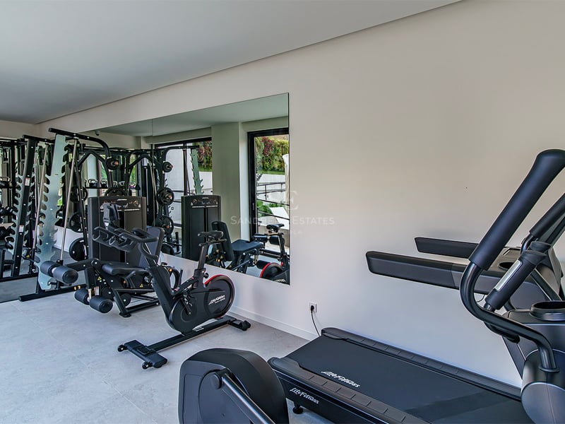 Salle de fitness moderne avec tapis de course, vélo et appareils de musculation devant un grand miroir.