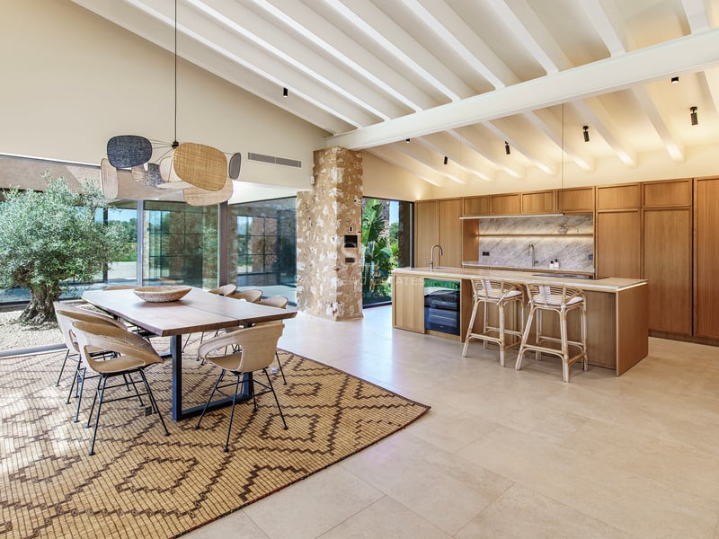 Cocina abierta con isla de madera, comedor contiguo, vigas blancas y pared de piedra natural.