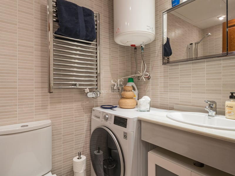 Salle de bains carrelée beige avec plan vasque en marbre, lave-linge et sèche-serviettes chauffant.