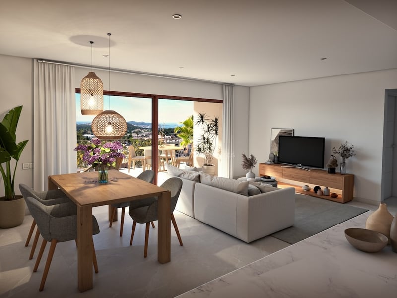 Bright open living room with a grey sofa, wooden dining table, and large glass doors opening to a scenic balcony view.