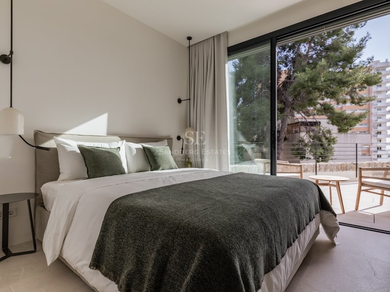 Chambre lumineuse avec lit double, coussins verts et grandes baies vitrées coulissantes ouvrant sur une terrasse.