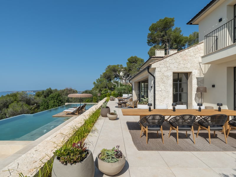 Terrasse de luxe avec piscine à débordement vue mer, salle à manger extérieure et façade en pierre naturelle.