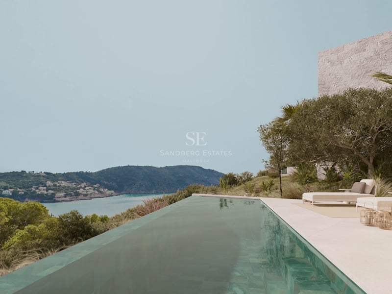Piscine à débordement sur une terrasse en pierre surplombant une baie turquoise et des collines verdoyantes.