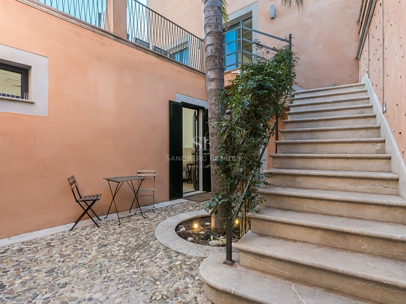 Cour privée aux murs pêche, sol en galets, escalier en pierre et table de bistrot.