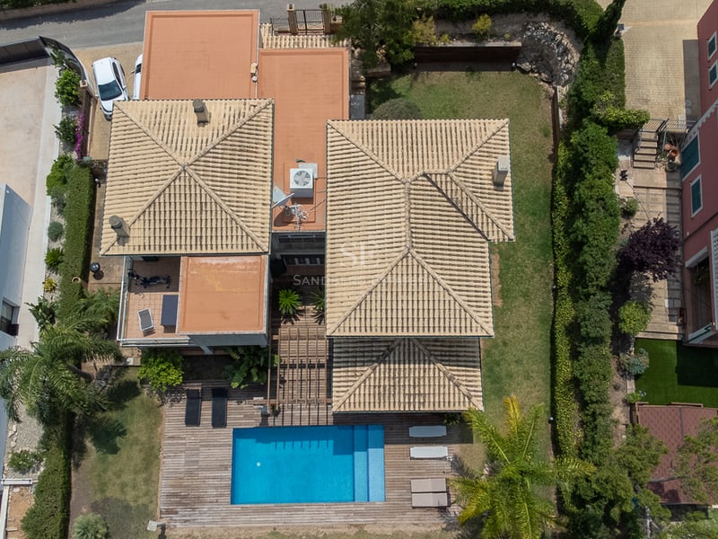 Vue de dessus d'une villa aux toits de tuiles beiges, piscine rectangulaire bleue et terrasse en bois avec jardin.
