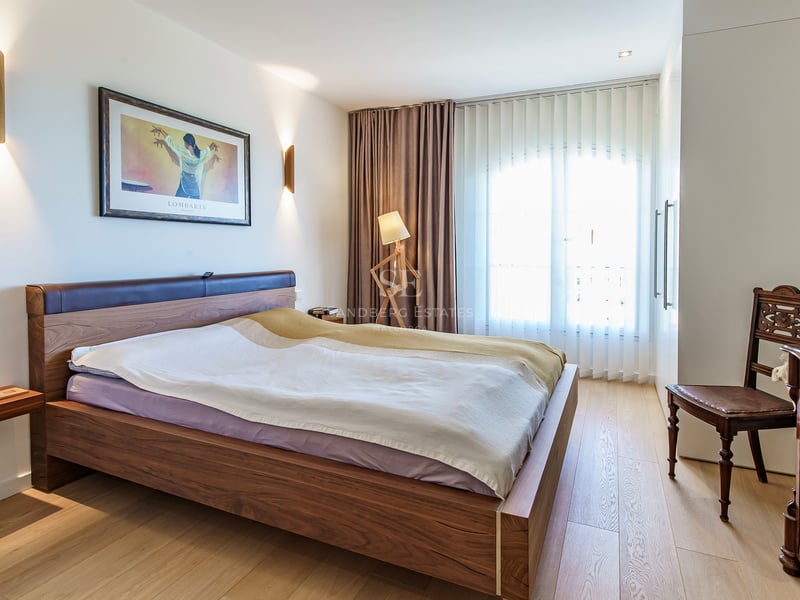 Chambre moderne avec cadre de lit en noyer, parquet en chêne clair et grande fenêtre avec voilages blancs.