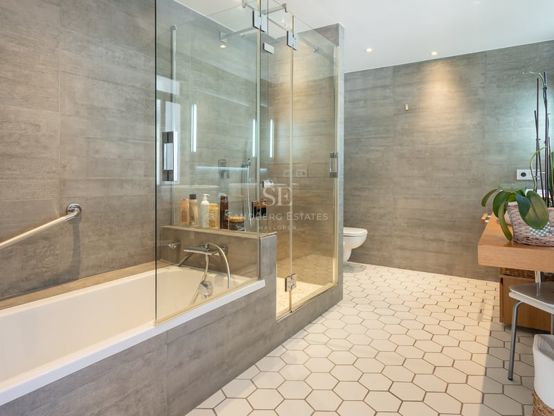 Salle de bain moderne avec carrelage hexagonal blanc, douche vitrée, baignoire et murs gris.