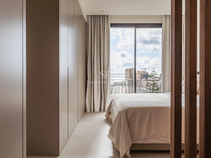 Chambre lumineuse aux tons neutres avec grand placard intégré et baie vitrée donnant sur la ville.