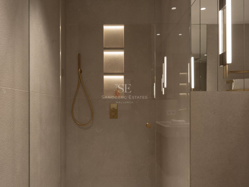 Douche en verre sans cadre avec carreaux de pierre couleur sable, éclairage encastré et robinetterie en or brossé.