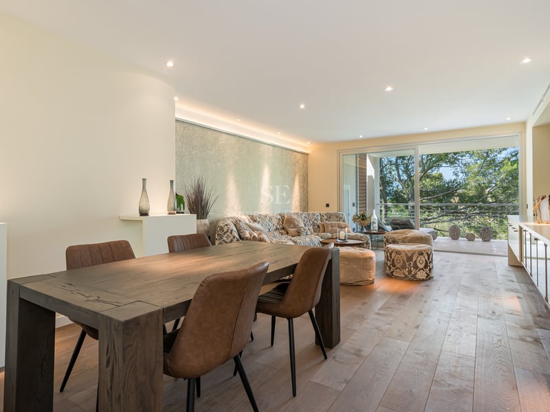 Espace de vie ouvert avec parquet en chêne, table en bois foncé et accès direct à une terrasse verdoyante.