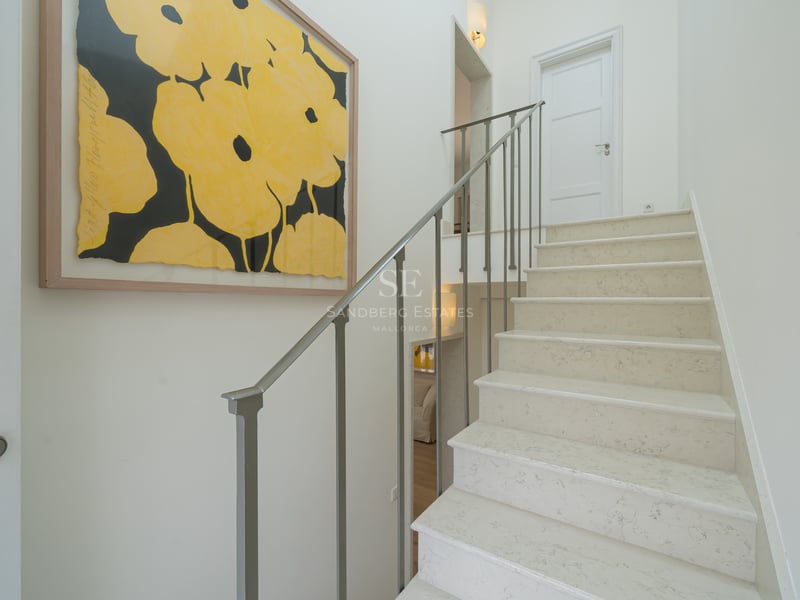 Escalier en pierre naturelle avec rampe fine en métal gris et tableau de fleurs jaunes sur mur blanc.