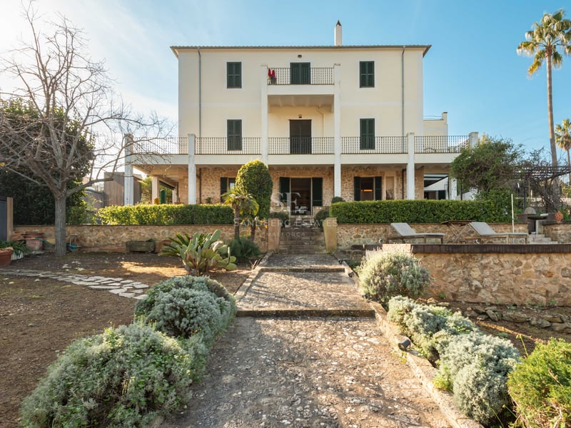 Vue d'une villa de trois étages avec détails en pierre, volets verts et chemin en pierre à travers le jardin.