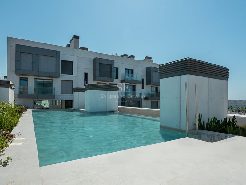 Piscine rectangulaire turquoise sur un toit-terrasse entourée de dalles en pierre et de bâtiments modernes.