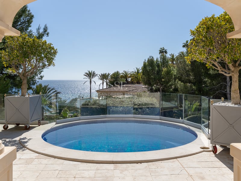 Piscine circulaire bleue sur une terrasse en pierre avec garde-corps en verre offrant une vue sur la mer.