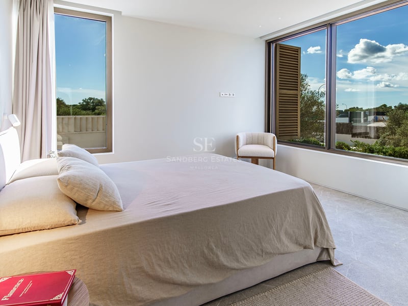 Chambre moderne lumineuse avec grande fenêtre sur jardin, sol en pierre naturelle et lit minimaliste.