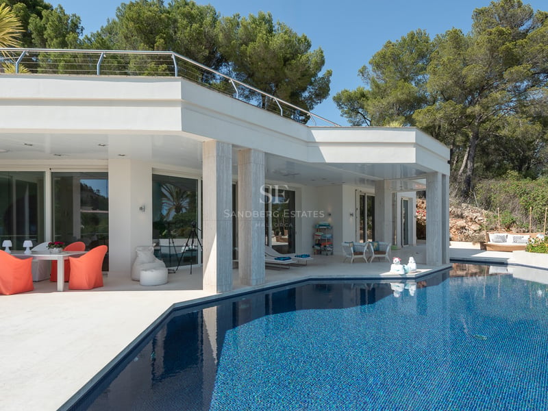 Vue extérieure d'une villa blanche moderne avec une grande piscine bleue et un coin repas ombragé.