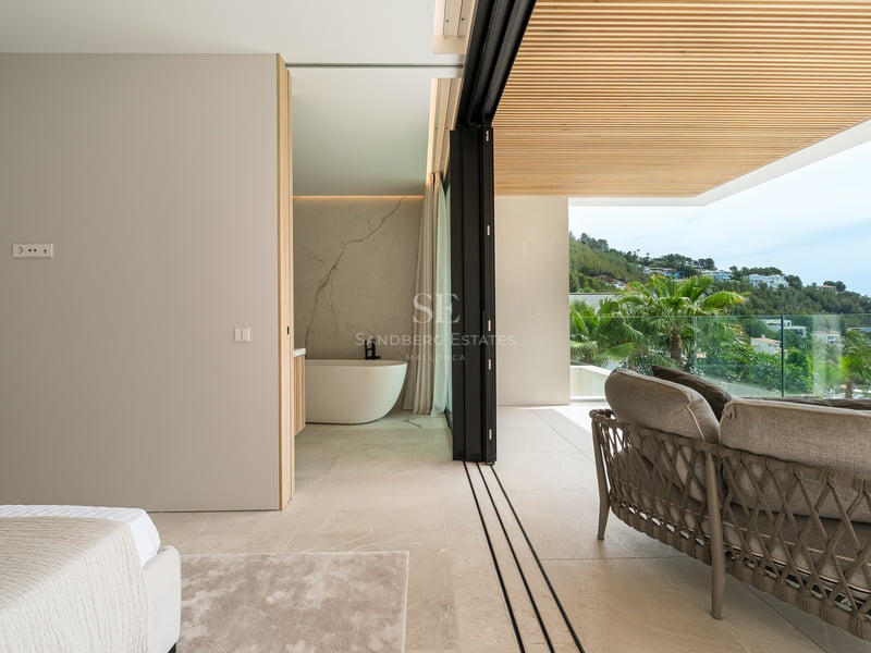 Chambre de luxe avec baignoire îlot et baies vitrées ouvrant sur une terrasse couverte avec vue sur les collines.