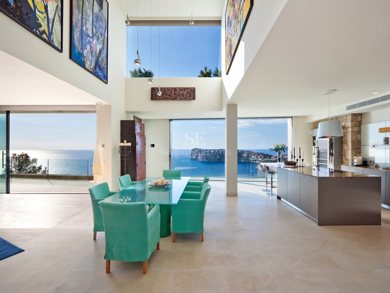 Salle à manger et cuisine modernes avec chaises turquoise et grandes baies vitrées offrant une vue mer panoramique.