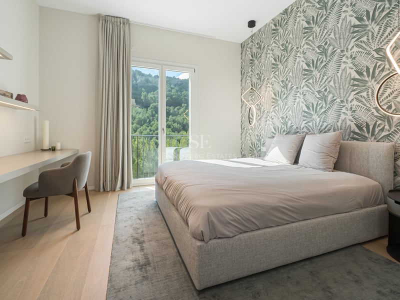 Chambre contemporaine avec papier peint botanique, lit rembourré, bureau intégré et balcon avec vue sur les collines.