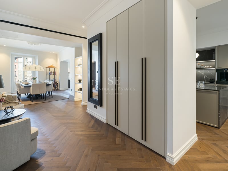 Modern open-plan apartment interior featuring oak herringbone floors, built-in storage, and a view of the dining area.