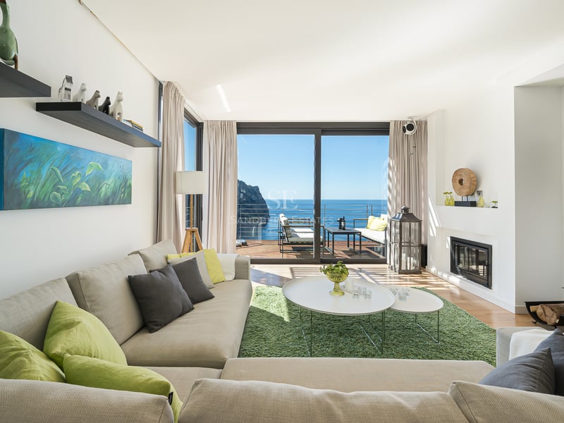 Salon moderne et lumineux avec de grandes baies vitrées ouvrant sur une terrasse vue mer et un canapé d'angle neutre.