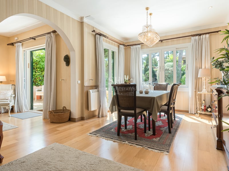 Salle à manger lumineuse avec lustre en cristal, meubles en bois sombre et portes-fenêtres ouvrant sur le jardin.