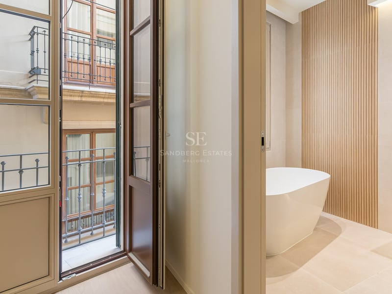 Modern bathroom with white freestanding bathtub, stone vanity, slatted wood wall, and balcony doors opening to a courtyard.