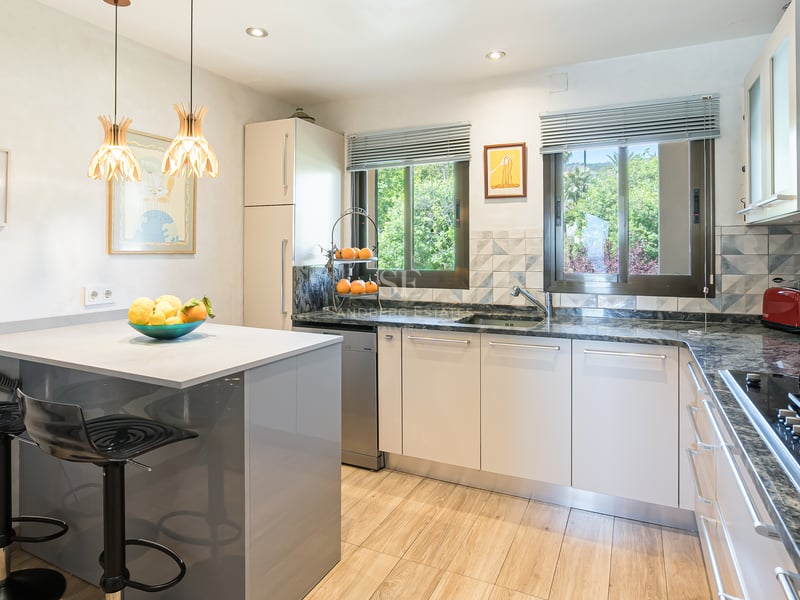 Cuisine moderne avec placards blancs, plans de travail en granit, îlot et fenêtres donnant sur la verdure.