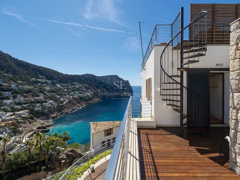 Terrasse avec parquet en bois et escalier en colimaçon surplombant une baie méditerranéenne et des montagnes.
