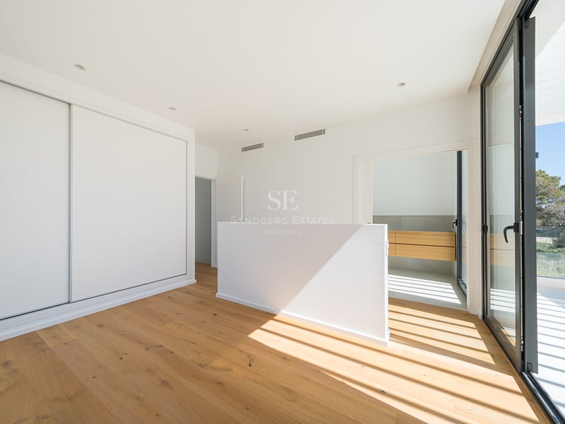 Chambre lumineuse avec parquet en chêne, placards blancs intégrés et grandes baies vitrées ouvrant sur une terrasse.