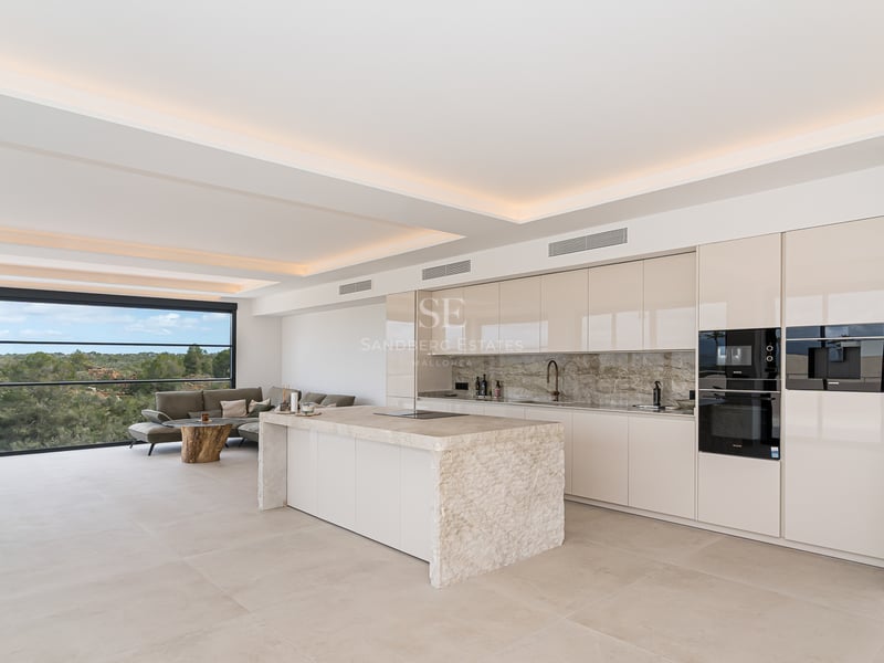 Cuisine blanche minimaliste avec un grand îlot en marbre, appareils intégrés et éclairage de plafond indirect.