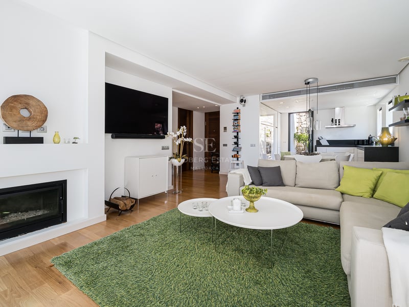 Salon lumineux avec parquet, canapé d'angle, cheminée intégrée et tapis vert dans un espace ouvert.