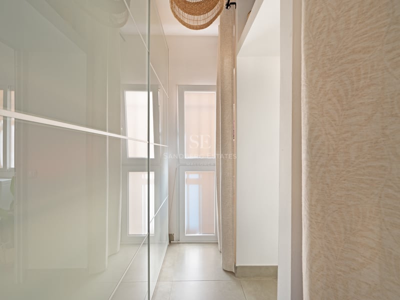 Couloir avec placards de plain-pied en verre dépoli, carrelage beige et suspension en osier.