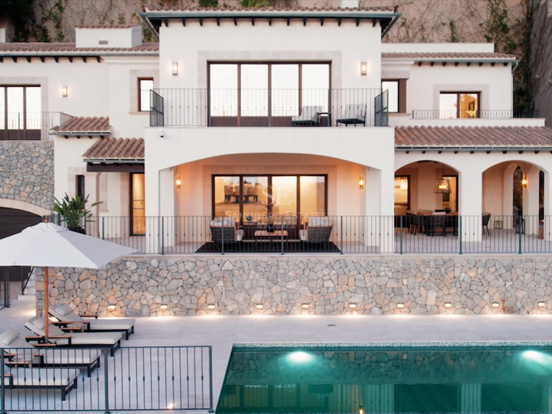 Vue de face d'une villa blanche à deux étages au crépuscule avec piscine et transats au premier plan.