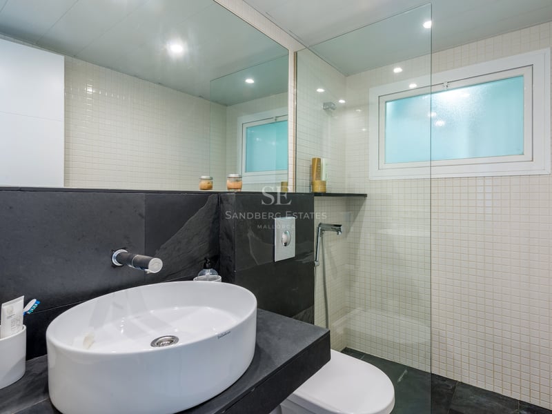 Salle de bain moderne avec vasque ovale blanche sur plan en ardoise foncée, mosaïque blanche et paroi de douche en verre.
