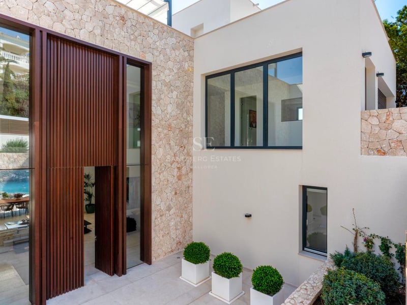 Entrée de villa moderne avec une haute porte en bois à lattes, des murs en pierre naturelle et un extérieur blanc.