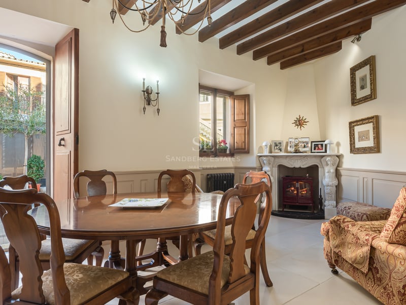 Salle à manger élégante avec table en bois, poutres apparentes et cheminée ornée menant à un patio.