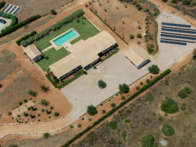 Vista aérea de una villa mediterránea con piscina, paneles solares y jardines en una gran parcela privada.