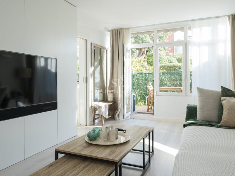 Salon moderne avec meuble TV blanc, table basse en bois et porte vitrée donnant sur une terrasse privée.