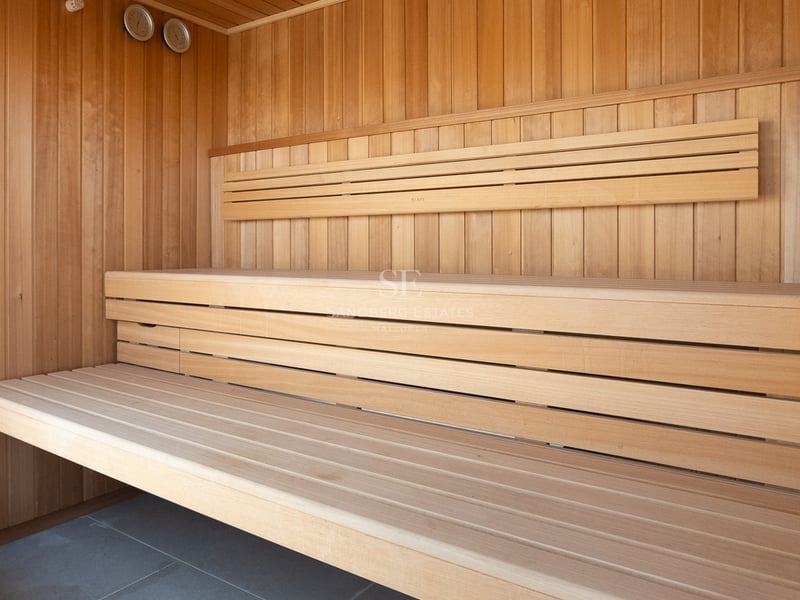 Sauna moderne en bois avec bancs à plusieurs niveaux et jauges de température intégrées sur un sol en pierre grise.