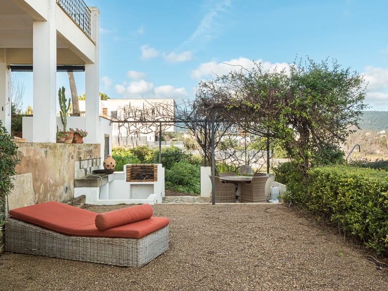 Terrasse avec bain de soleil orange, barbecue maçonné et coin repas sous une pergola verdoyante.