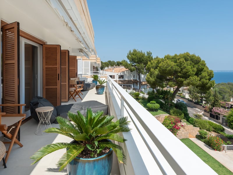 Longue terrasse avec volets en bois, mobilier lounge et vue panoramique sur la mer et la végétation.