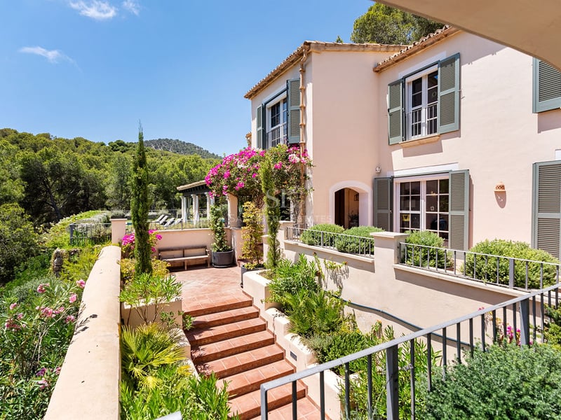 Villa couleur pêche avec volets verts et terrasse en terre cuite surplombant une vallée boisée ensoleillée.