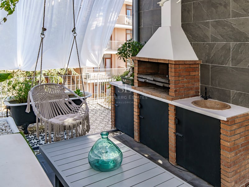 Terrasse moderne avec barbecue en briques, fauteuil suspendu en macramé, table et carrelage décoratif.