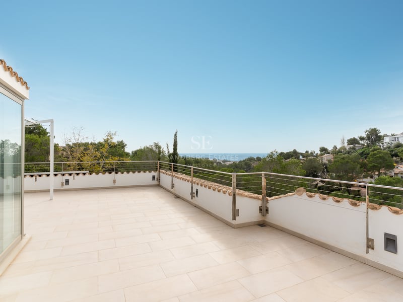 Grande terrasse carrelée avec rambarde métallique offrant une vue dégagée sur la mer et la végétation.