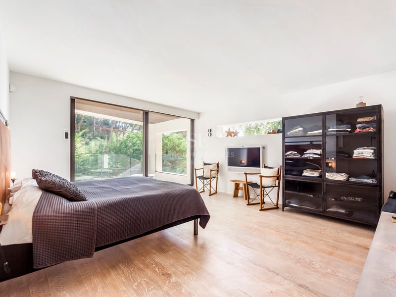 Chambre contemporaine lumineuse avec parquet en chêne, baies vitrées et armoire industrielle en verre noir.