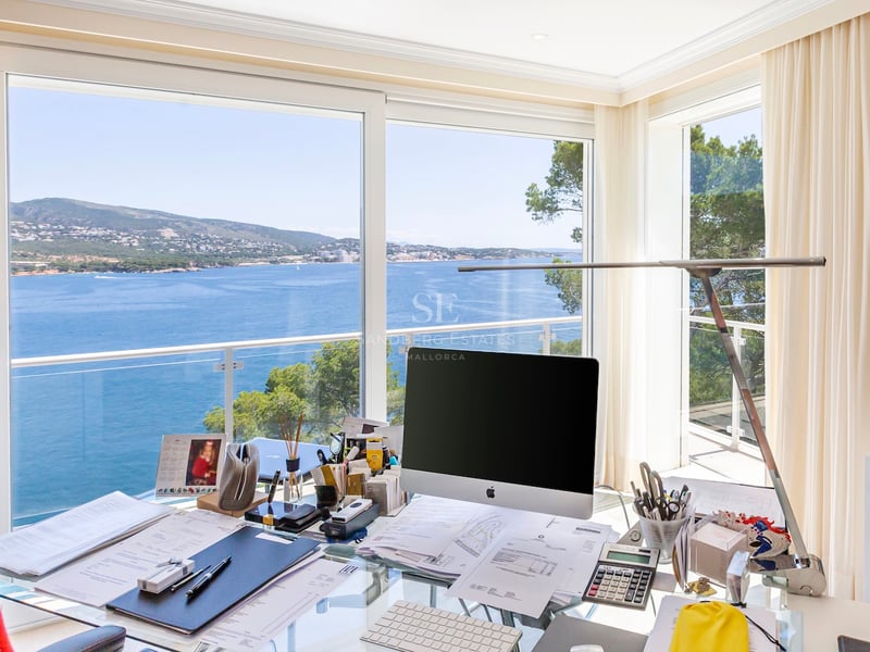 Bureau moderne avec table en verre et ordinateur devant une vue imprenable sur la mer bleue et la côte méditerranéenne.