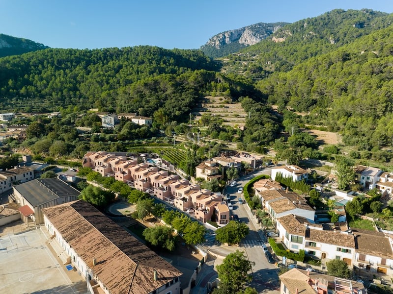 Vue aérienne par drone montrant des maisons modernes en terre cuite dans un village méditerranéen entouré de montagnes.